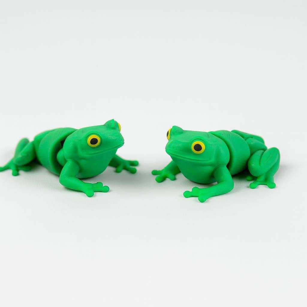 Two 3D printed tiny frog desk buddies facing each other on a white background